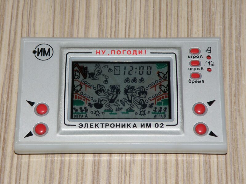 Šedá kapesní hra Elektronika IM-02 se čtyřmi červenými směrovými tlačítky a motivem vlka na displeji.