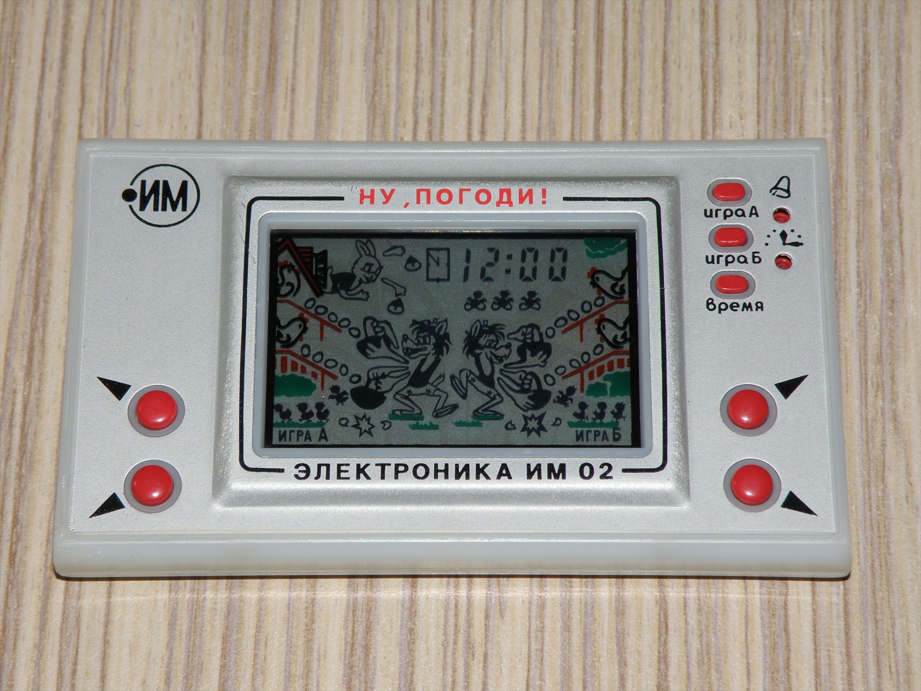 Šedá kapesní hra Elektronika IM-02 se čtyřmi červenými směrovými tlačítky a motivem vlka na displeji.