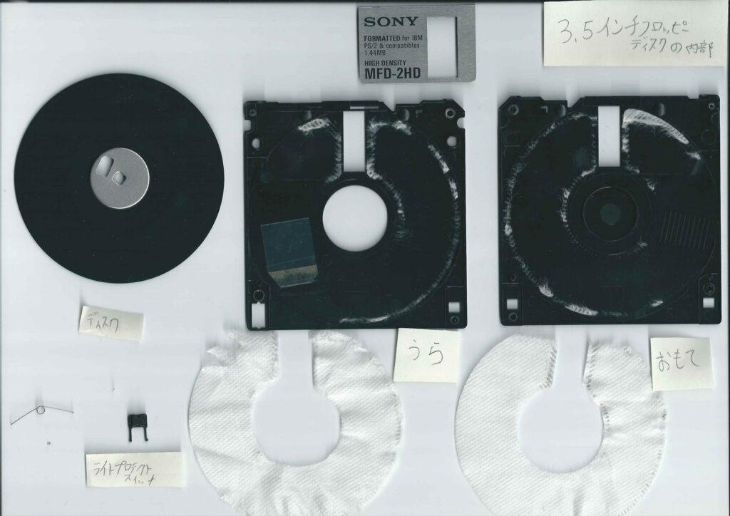 Součásti rozebrané diskety Sony: magnetický kotouč, dvě poloviny pouzdra, kovová krytka a bílé vnitřní výstelky.