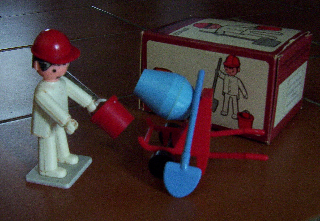Plastová retro figurka Igráček v podobě stavaře s helmou, lopatou a kbelíkem na podložce.