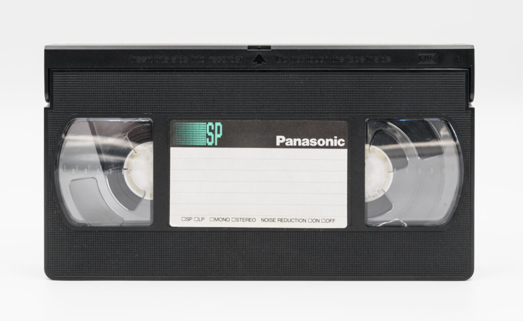 Detailní pohled na černou videokazetu formátu VHS položenou na světlém pozadí.