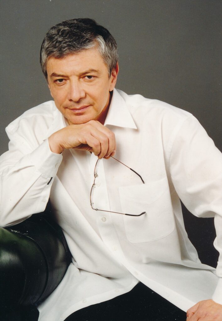 Vladimír Železný sedí v bílé košili v křesle a drží brýle, portrét z roku 2000