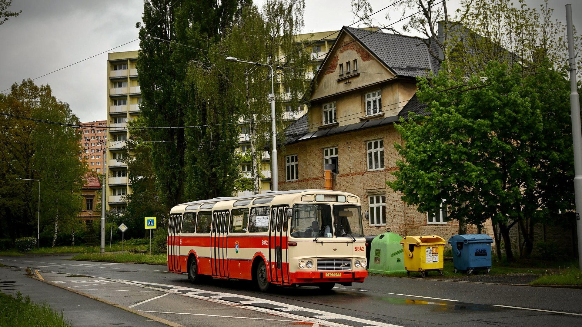 Červenobílý městský autobus Karosa ŠM 11 projíždějící ulicí se sídlištěm v pozadí
