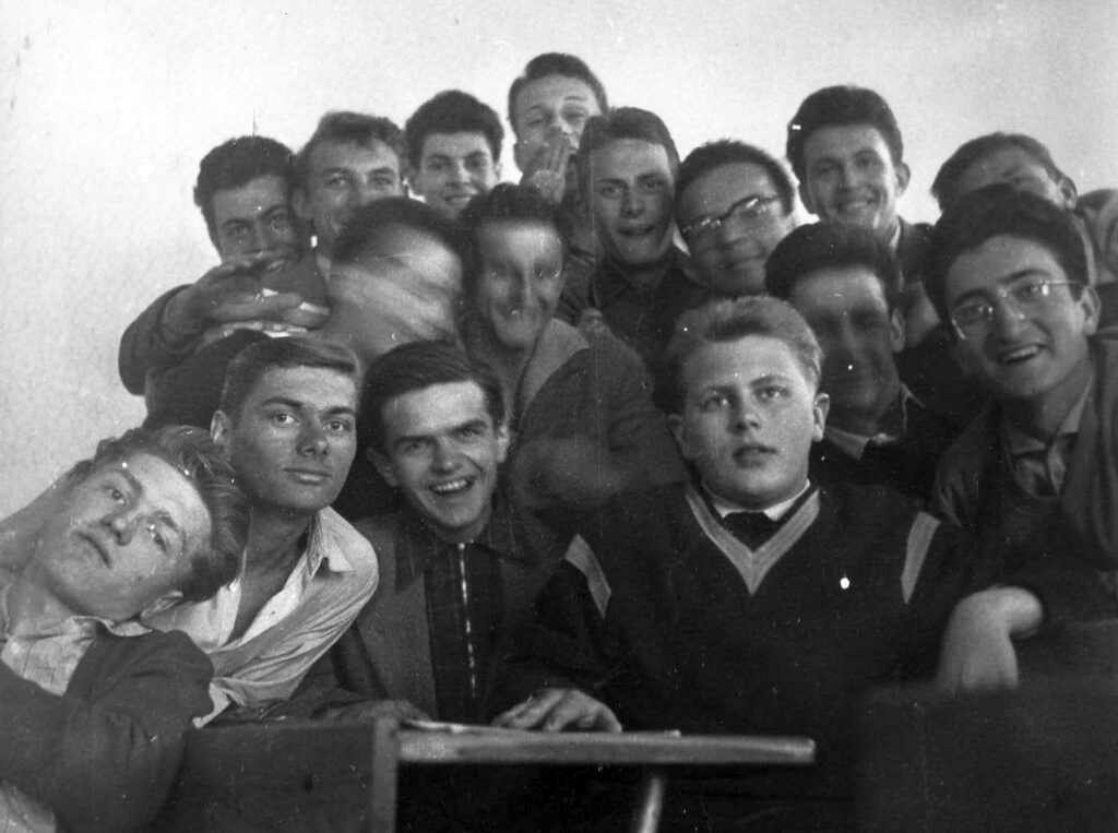Dva usmívající se školáci sedící za dřevěnou lavicí se sešity a školními pomůckami.
