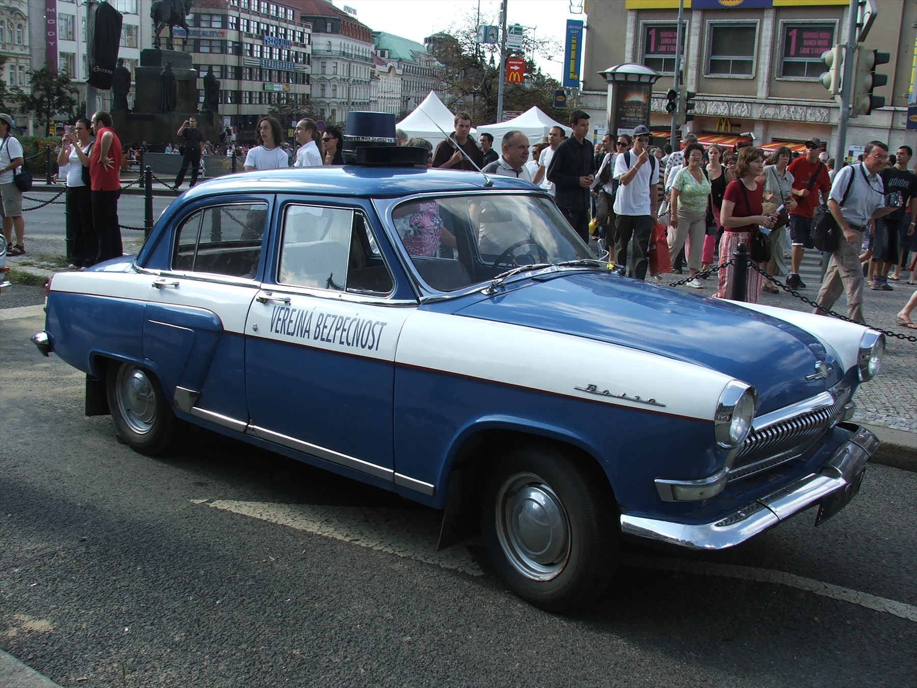 Modrobílý osobní automobil GAZ-21 Volha s nápisem Veřejná bezpečnost na dveřích a majákem na střeše