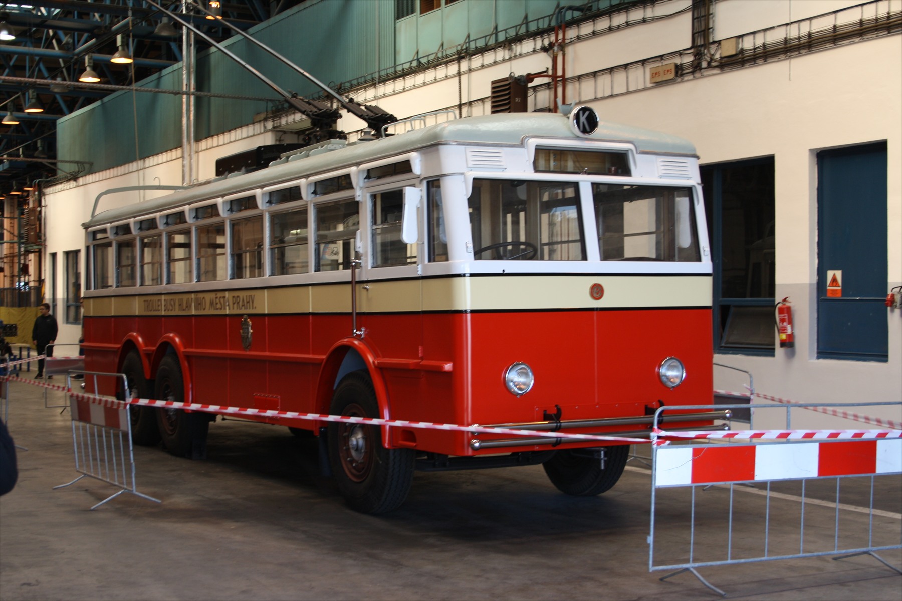 Červenokrémový historický trolejbus Praga TOT s označením linky K vystavený v hale.
