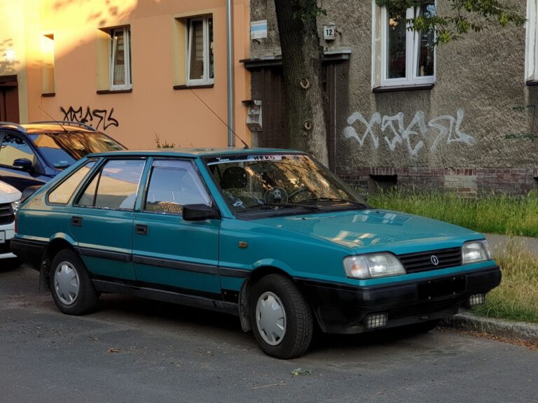 Červený osobní automobil FSO Polonez Caro s plastovými nárazníky a hranatými světlomety zaparkovaný na ulici.
