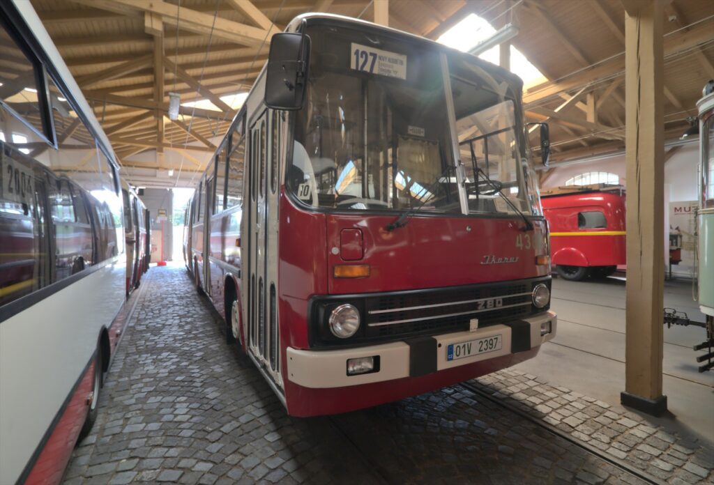 Červeno-bílý kloubový autobus Ikarus 280 s harmonikovým měchem a otevřenými dveřmi v areálu vozovny.