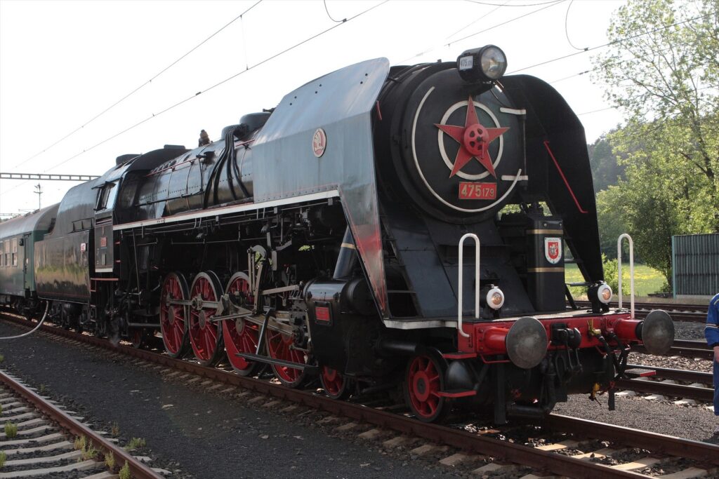 Parní lokomotiva 475.179 s červenými koly a tendrem na koleji.