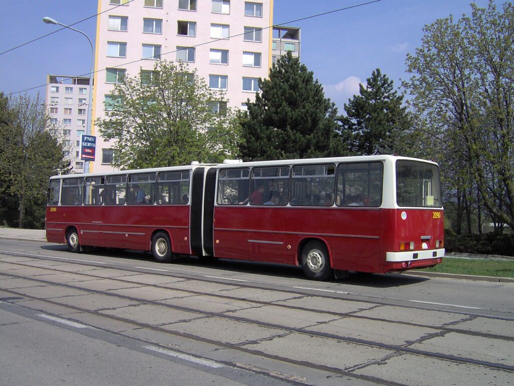 Kloubový autobus Ikarus 280 v ulici města s natočeným kloubem během průjezdu mírným obloukem.