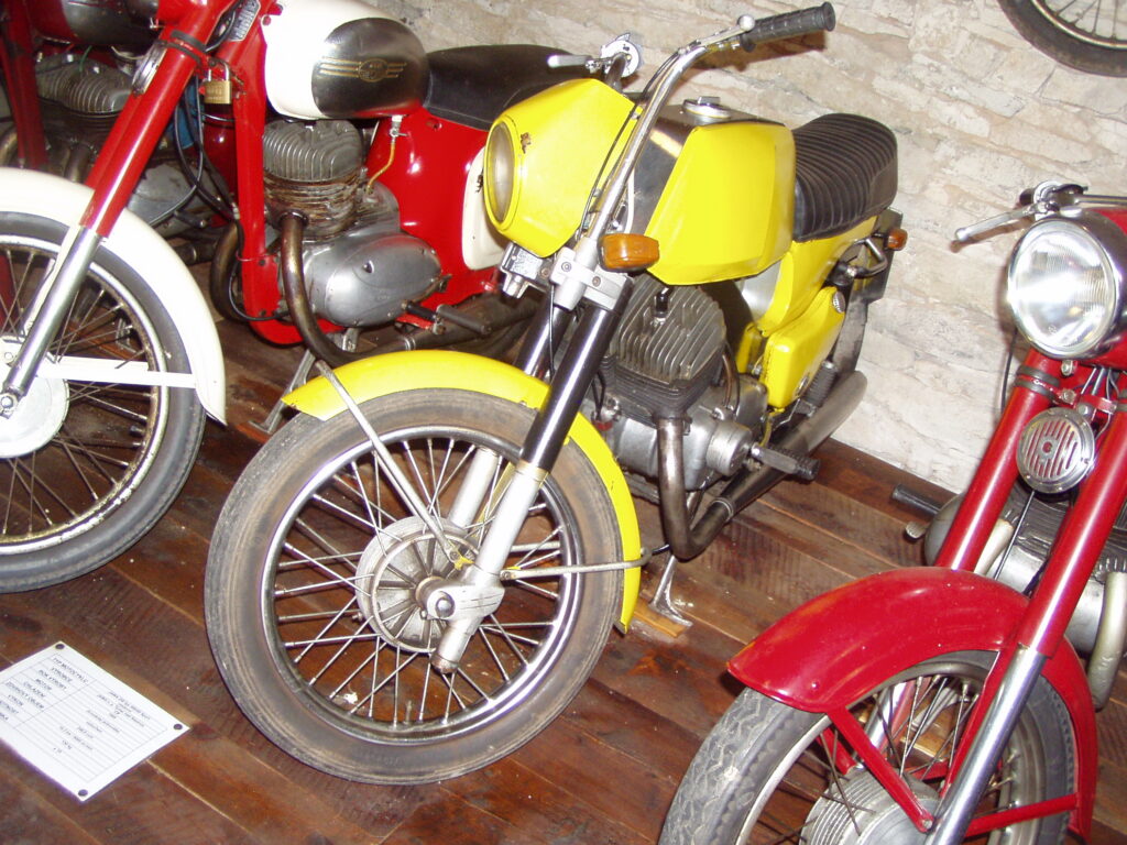 Žlutá Jawa 350 Bizon mezi dalšími motocykly, s dlouhými trubkami řídítek vedle světlometu.