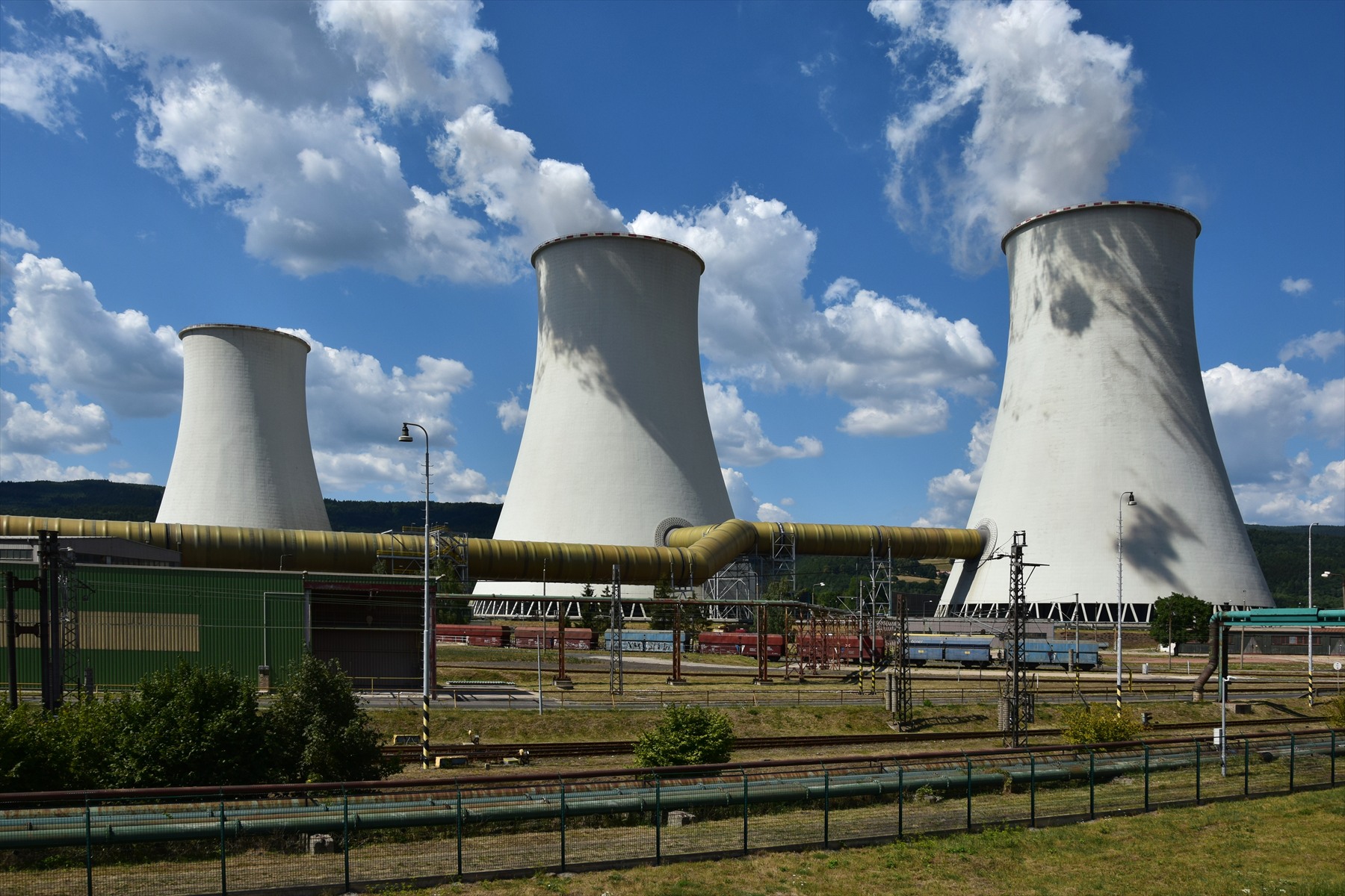 Areál uhelné elektrárny s mohutnými chladicími věžemi, kouřícími komíny a technologickými budovami pod Krušnými horami.