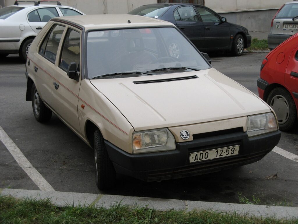 Hnědý pětidveřový hatchback Škoda Favorit 136 L s asymetrickou přední maskou chladiče zaparkovaný na ulici.