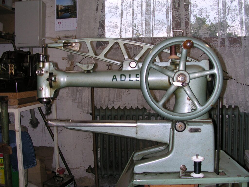 Masivní mechanický obuvnický šicí stroj značky Adler s ramenem pro sešívání kožených dílců obuvi.