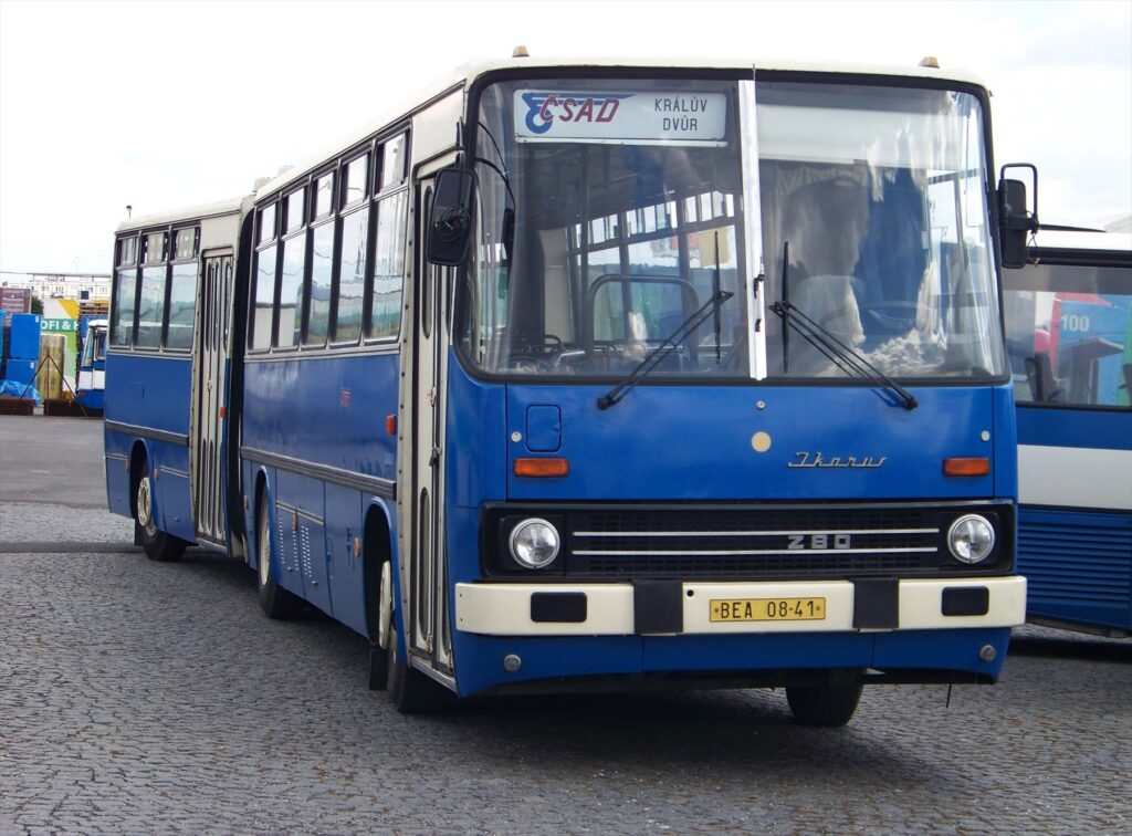 Modro-bílý linkový kloubový autobus Ikarus 280 s dvojicí dveří a bočními okny na parkovací ploše.