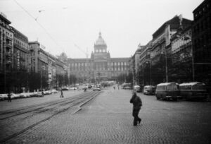 Koleje středem Václavského náměstí, chodci a zaparkovaná vozidla před Národním muzeem.