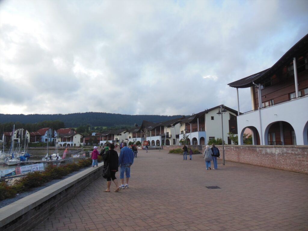 Lidé na promenádě u přístavu s plachetnicemi v Lipně nad Vltavou.