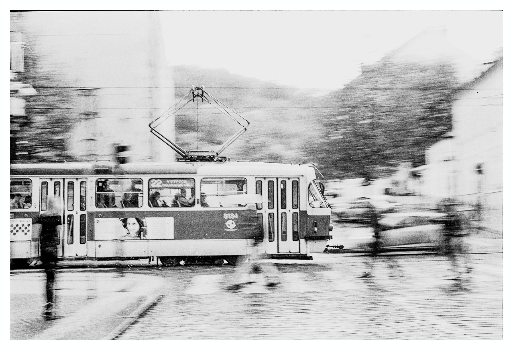 Černobílá fotografie projíždějící pražské tramvaje s rozmazaným pozadím.