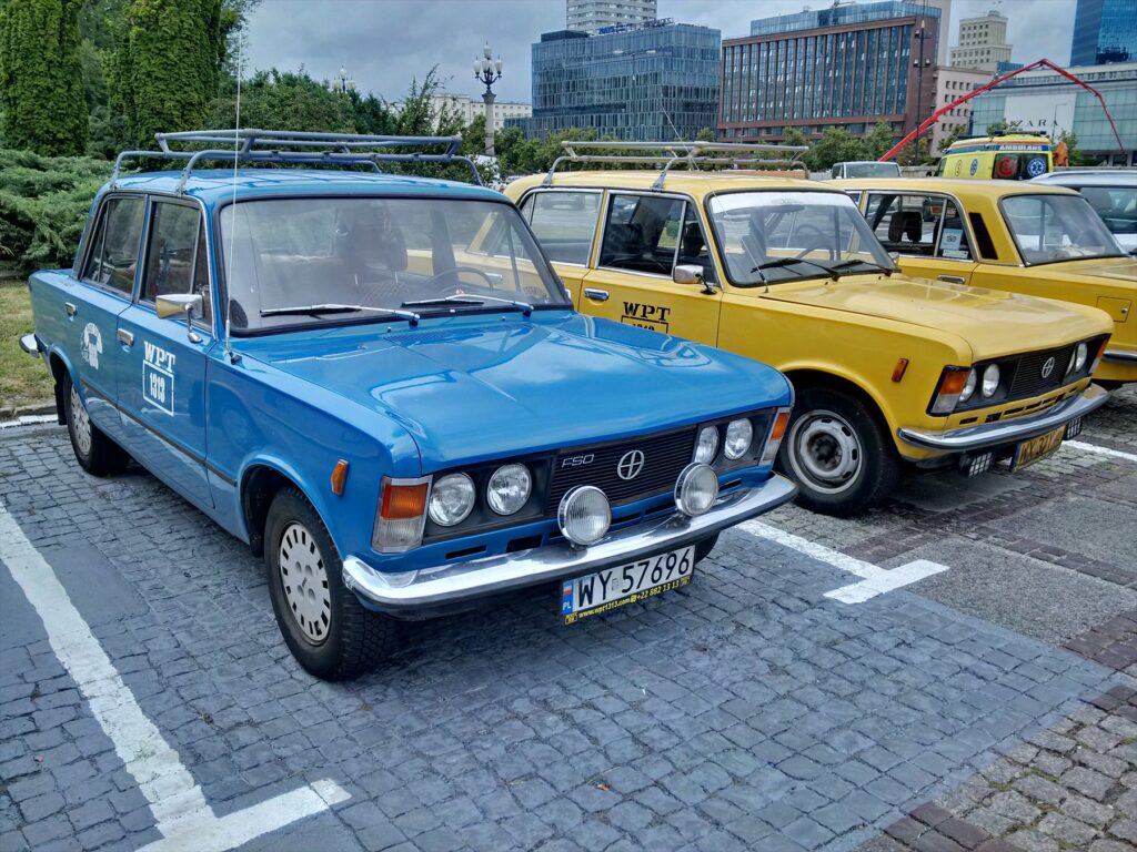 Červený historický sedan Polski Fiat 125p se čtyřmi kruhovými světlomety a chromovanou maskou.