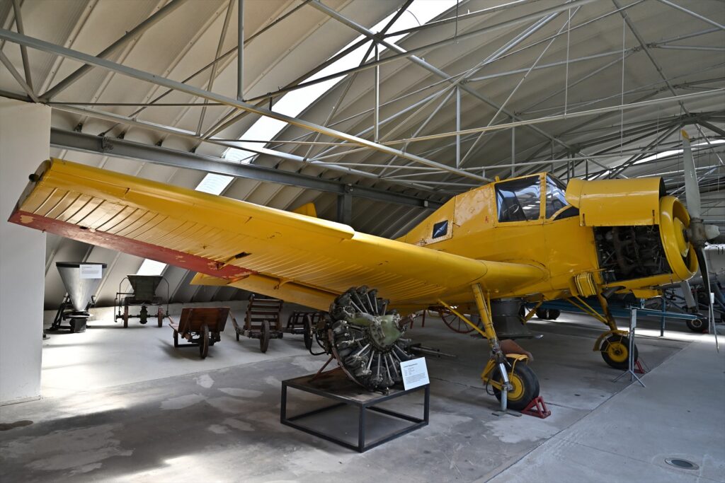 Žlutý zemědělský Z-37 s otevřeným krytem motoru je vystaven v hale mezi historickými stroji.