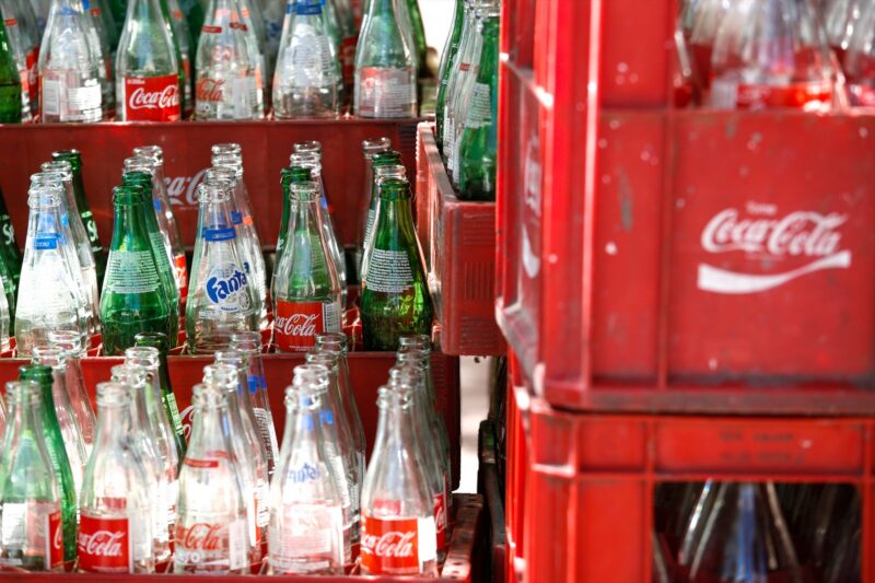 Řada klasických skleněných lahví Coca-Cola s korunkovými uzávěry v dřevěné přepravce
