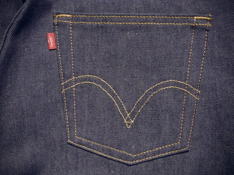 Detail zadní kapsy klasických džínových kalhot z tmavého denimu s prošíváním a červenou etiketou