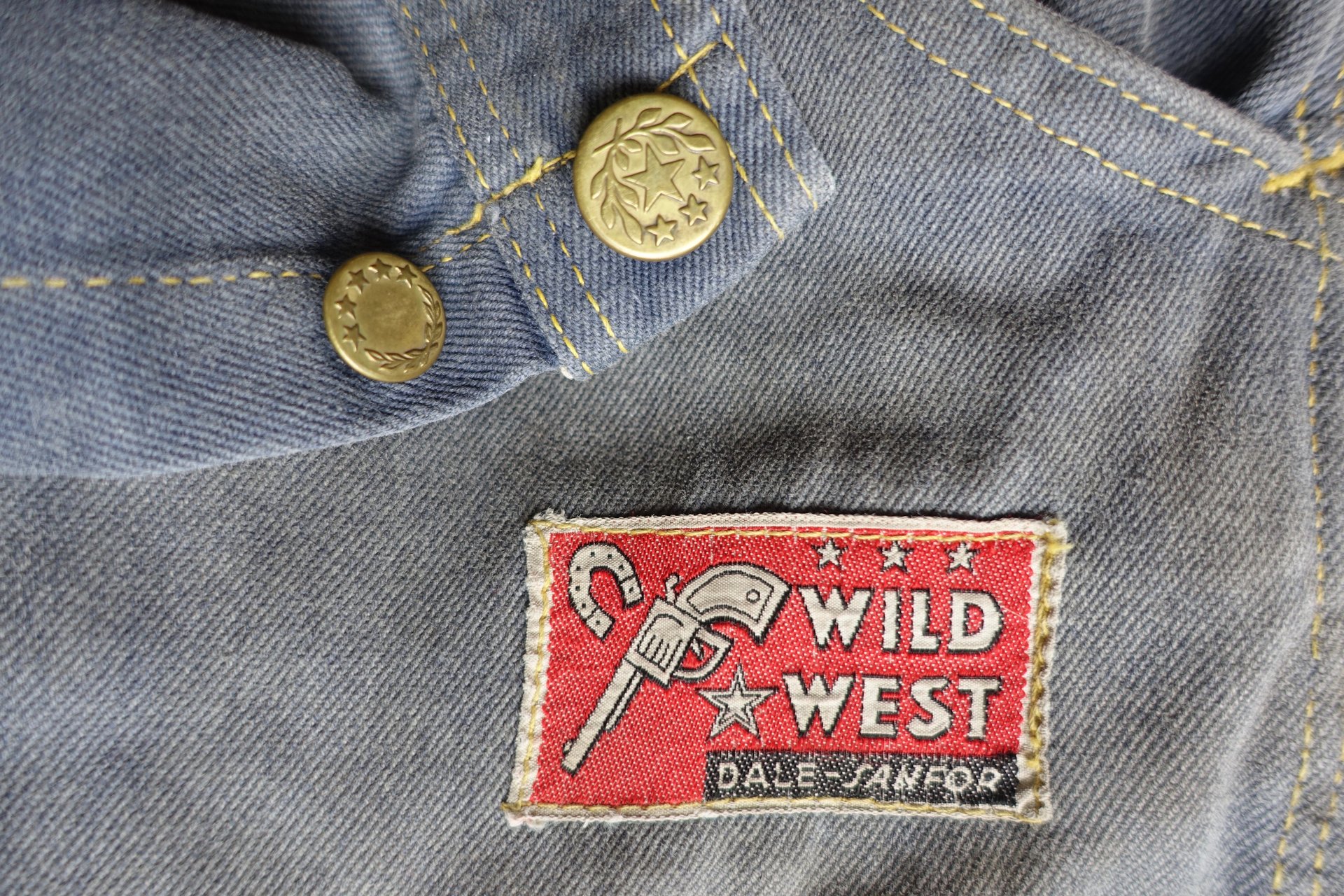 Detail dobových kalhot z bavlněného kepru s kovovými knoflíky a westernovou nášivkou Wild West