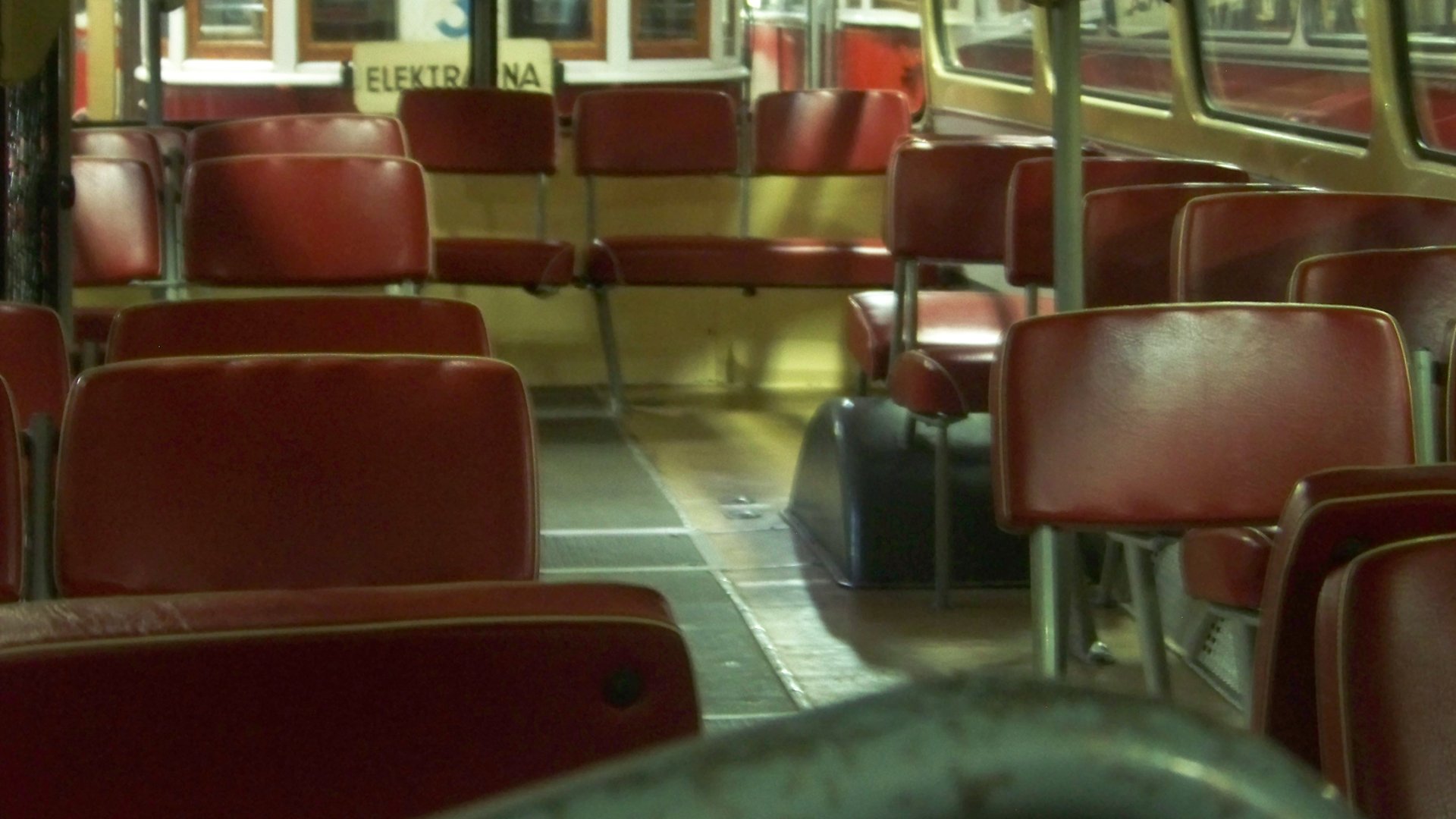 Pohled do uličky autobusu Karosa ŠM 11 s červenými koženkovými sedadly a stropními madly