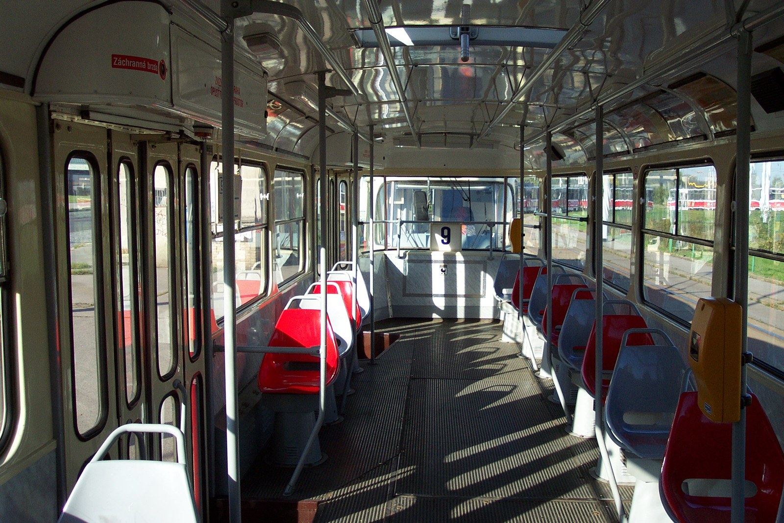 Interiér tramvaje Tatra T3 s řadou tvarovaných laminátových sedaček a madly podél uličky.