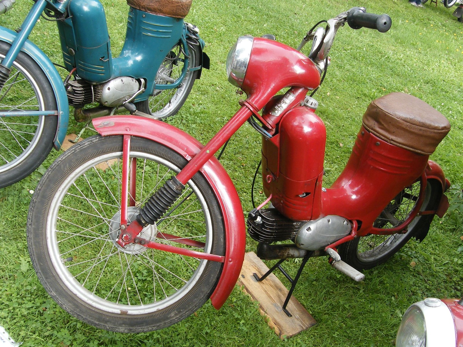 Historický červený moped Jawa 50 typ 550 Pařez s jednodílným sedlem v trávě.