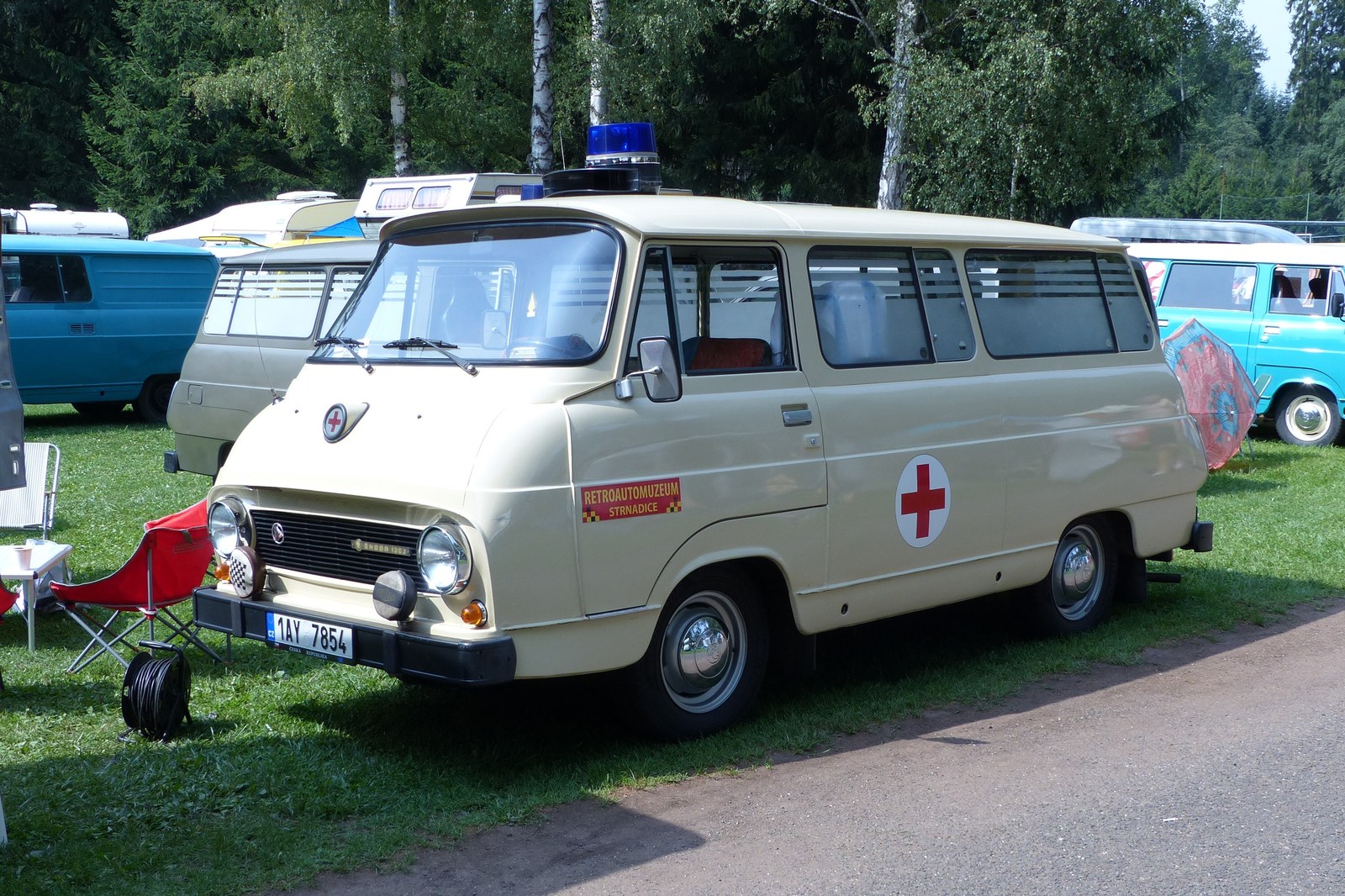Bílá sanitka Škoda 1203 s červeným pruhem, modrým majákem na střeše a označením rychlé lékařské pomoci.