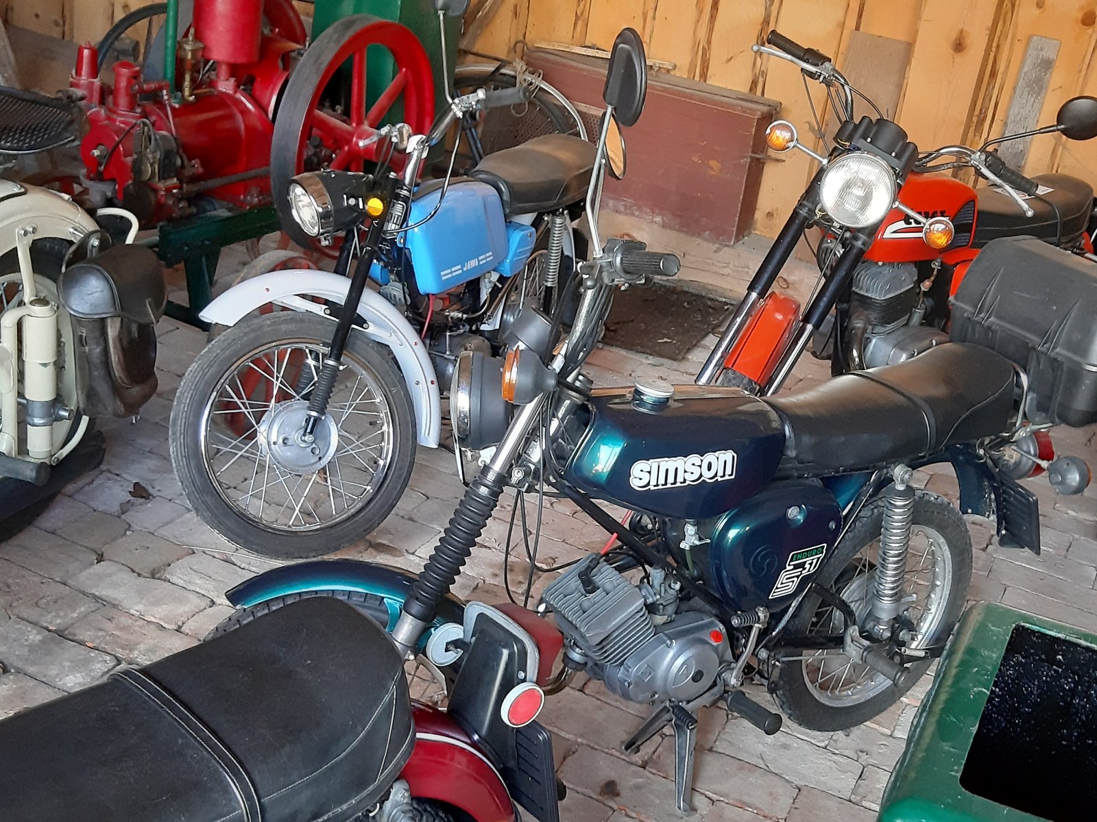 Červený lehký motocykl Simson S51 zaparkovaný před dřevěnou venkovskou budovou