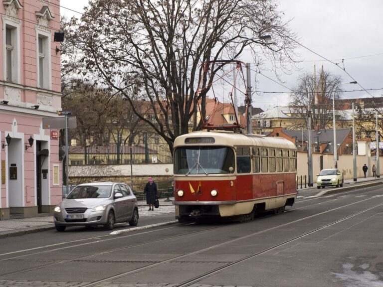 Červeno krémová tramvaj Tatra T3 projíždějící křižovatkou s pantografem na střeše.