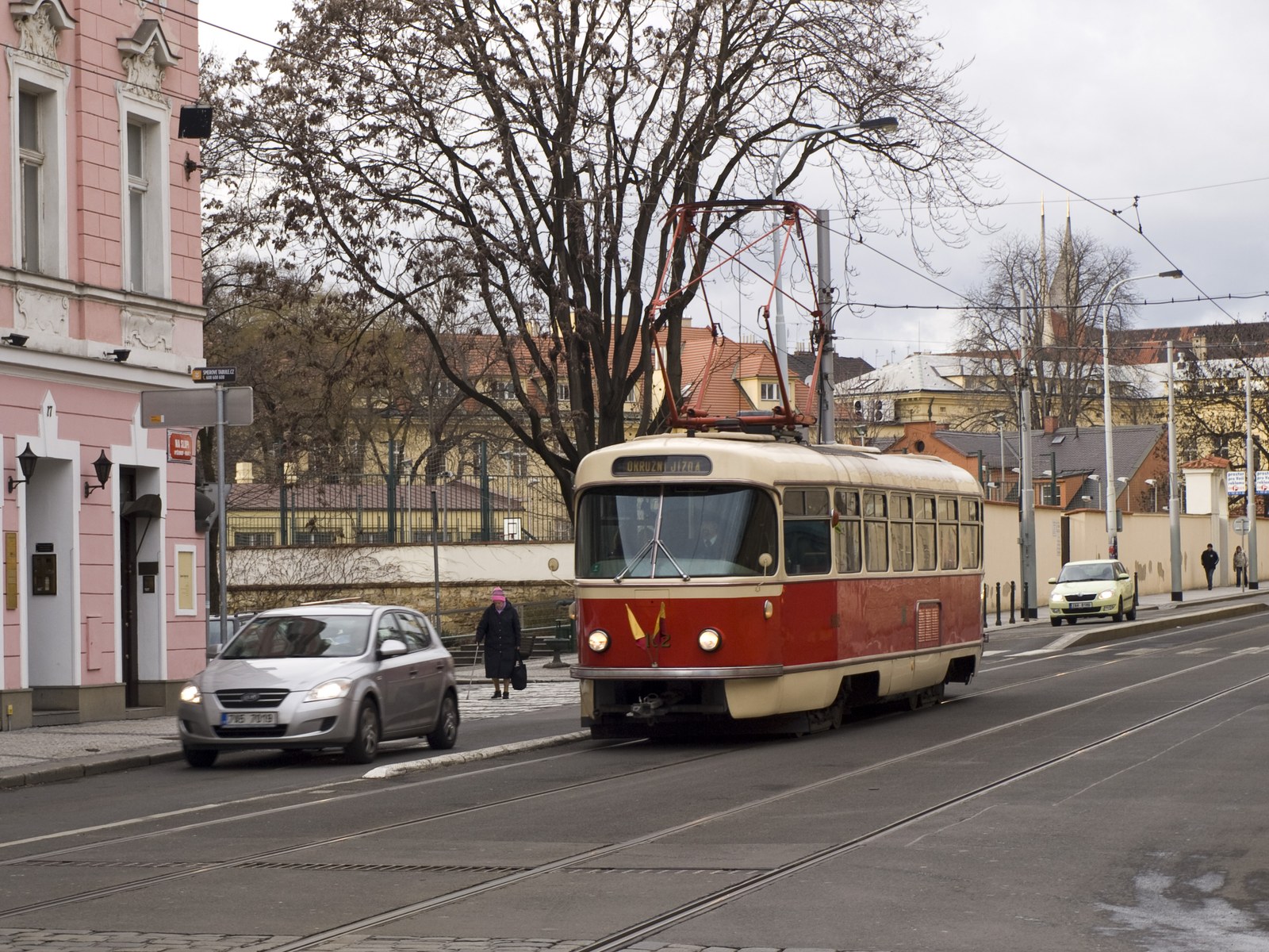 Červeno krémová tramvaj Tatra T3 projíždějící křižovatkou s pantografem na střeše.
