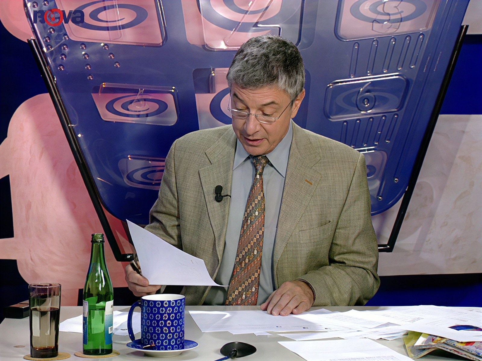 Vladimír Železný s brýlemi čte z papíru před kulisou s emblémy Novy